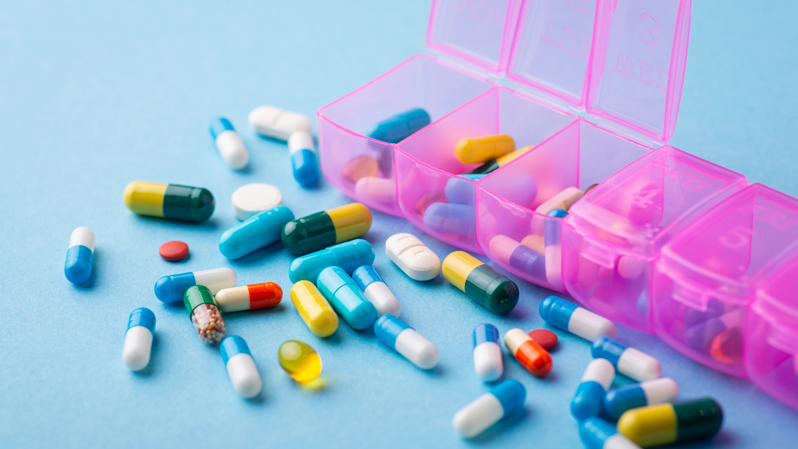 Colorful prescription pills and a weekly pill organizer on a table, representing how women often manage multiple medications instead of addressing root‑cause metabolic health.