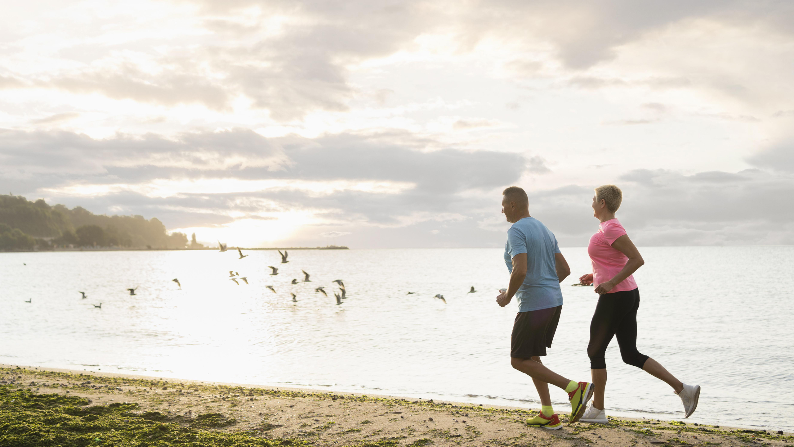 A mature couple jogging along the shoreline on a bright morning, enjoying relaxed weekend movement and outdoor exercise.