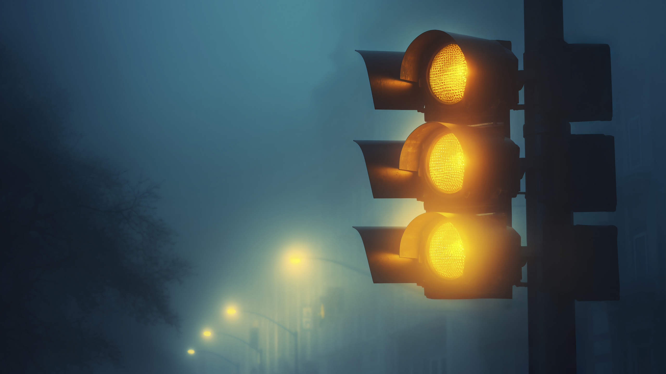 A yellow traffic light shining through dense nighttime fog with a soft yellow glow.