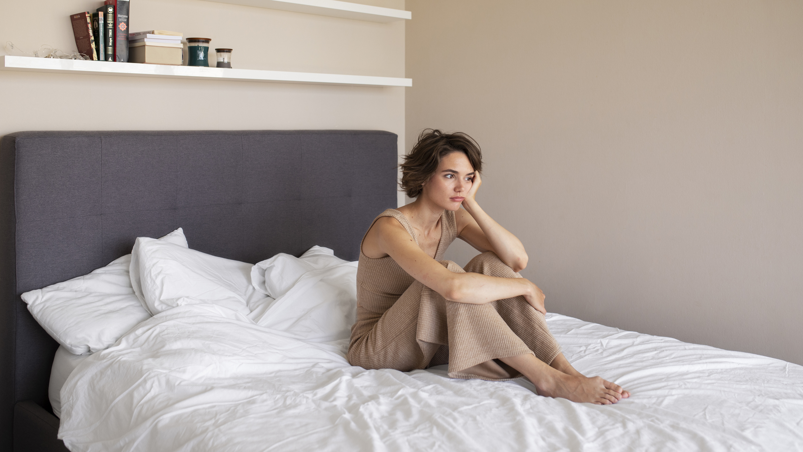 Woman sitting in bed looking tired with knees drawn up, showing morning fatigue and emotional exhaustion.
